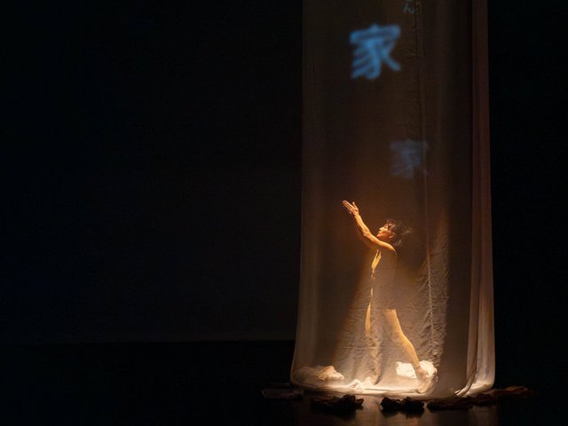 A mostly dark image with the light focused on a dancer to the right of the image.
