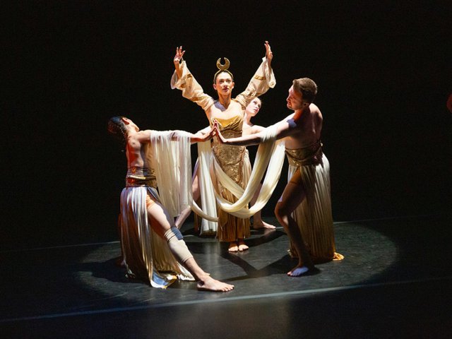 A woman raises her hands high surrounded by a ring of other dancers.