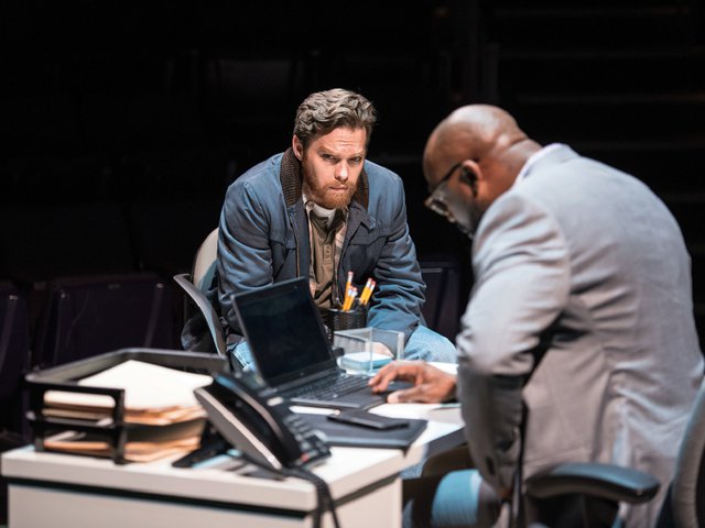 Two men huddle over a desk.